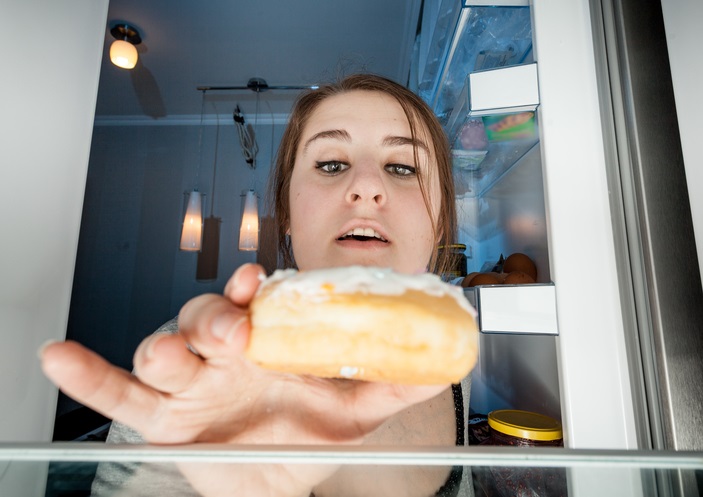 portrait of woman taking donut from fridge